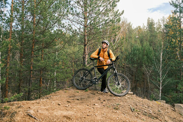 a male cyclist in a protective helmet stopped in the autumn forest and enjoys nature