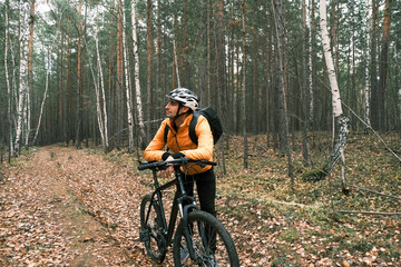 Fototapeta premium a male cyclist in a protective helmet stopped in the autumn forest and enjoys nature