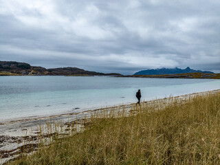 tourist woman walking on sand of mjelle beach during autumn with cyan water and mountains on background