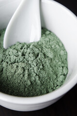 Green bentonite clay powder in a bowl. Clay texture close-up. Diy mask and body wrap recipe. Natural beauty treatment and spa.