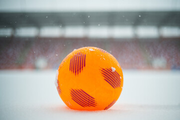 Orange soccer ball lying on the snow at football pitch