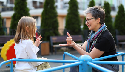 Joyful woman and daughter communicate in sign language outdoors, fostering love, happiness, and cultural connection. © Andrii Zastrozhnov