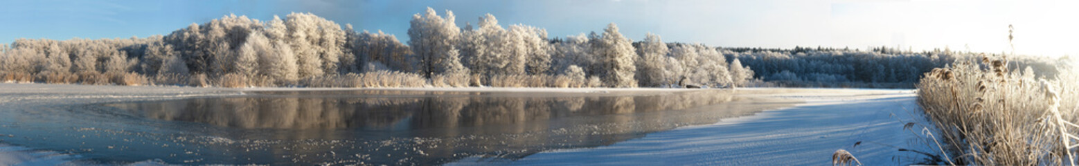 Panorama view of river partly covered in ice with reflection of snow covered trees