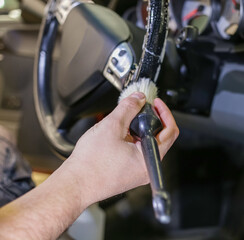 A man cleans the steering wheel of a modern car using a special brush. Dry cleaning of the car interior, close-up, selective focus. Car detailing and the concept of car interior care.