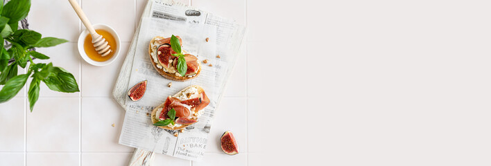 Delicious Bruschetta banner. Crostini with prosciutto, ricotta, figs, basil, walnut and honey on a wooden board. Antipasti, canape, crostini recipe, restaurant menu. Tasty breakfast. Copy space