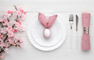 Easter holiday table setting with egg on plate and cutlery, sakura blossom, pink spring flowers....