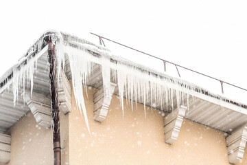 Carefully. Danger. Beautiful sharp icicles and snow hang from the eaves of the roof. Transparent...