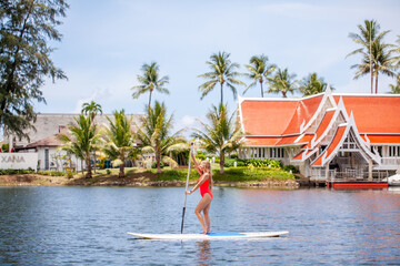 Woman paddleboarding on tranquil water near tropical resort. Water sports and vacation.