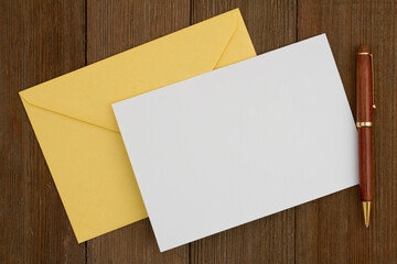 Blank greeting card with yellow envelope and pen on wood