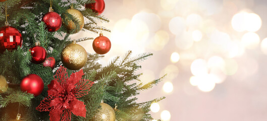 Christmas tree decorated with red and golden festive balls against blurred background, bokeh effect. Banner design with space for text