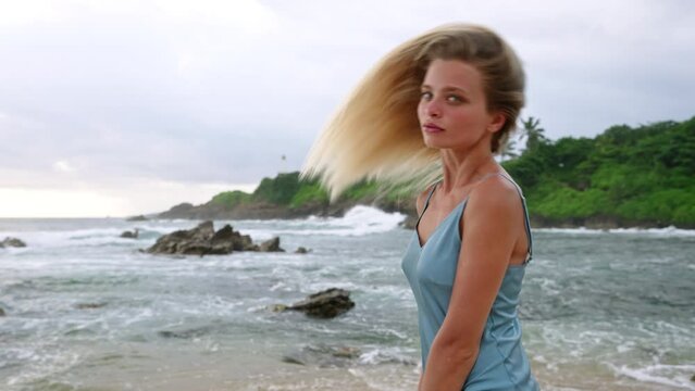 Blonde woman flips long hair on tropical beach backdrop. Beauty model showcases lustrous locks by sea. Haircare promo with natural ocean setting. Healthy hairstyle in motion, coastal lifestyle.