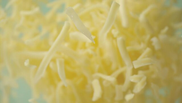 Heap grated cheddar cheese flying in slow motion close up. Shredded yellow parmesan cheese falling in macro. Ungraded raw ProRes footage for grading