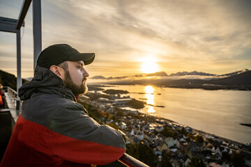 pensive young man against the background of the rising sun over the city of alesund at the aksla...
