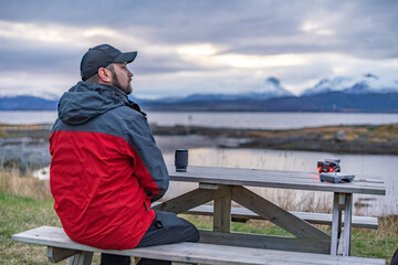 A male tourist sits at a wooden table with photo and video equipment, including a drone, on the...