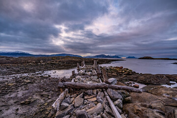 old wooden stone pier during tide on shore of bodo in norway with mountains on background