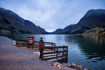 man tourist with beard on wooden pier with lifebuoy behind with mountain Sandvevatn lake behind