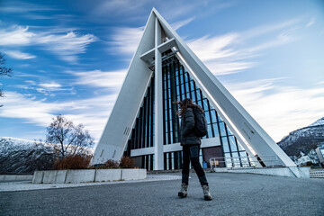 young pretty woman poses in front of arctic Cathedral church in tromso during winter