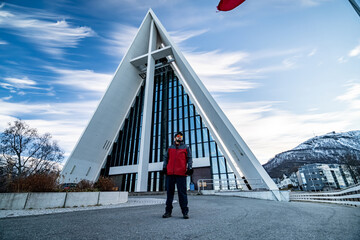 young man with beard stands in front of arctic cathedral in tromso, norway