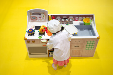 A toddler girl pretends to be a chef in a play kitchen. 