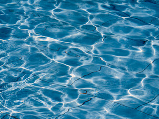 The water in the outdoor pool is agitated, the curved reflections of the sun on the surface of the water create a beautiful abstract picture, natural abstract texture
