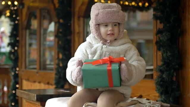 Little girl at the Christmas market. The child is holding a box with a present in her hand. The little girl tries to open the present.