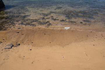 Seascape, white sandy beach with turquoise blue water with white plastic bag in the water. Lanzarote, Canary Islands, Spain.
