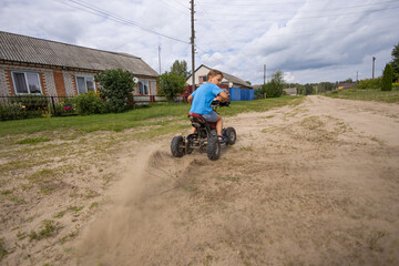 A child rides along a sandy road on an ATV. Quad bike. The wheels of the ATV roll along the dirt...