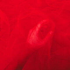 women's hand with red elastic fatin fabric tulle mesh. for sewing wedding and masquerade dresses.