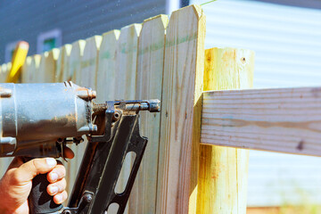 By using an air nail gun, he constructs sections of wooden fence around his yard - obrazy, fototapety, plakaty