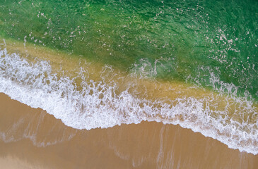 Aerial view of waves crashing on sandy shore, surface ocean waves beach