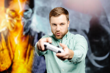 Young bearded man standing at the wall in the room and playing, holding wireless joystick, screaming, and winning intense video game match