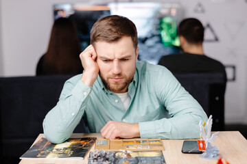 Man with board game piece while practicing strategy in home alone. A man plays a board game with cards and figures, expressing different emotions