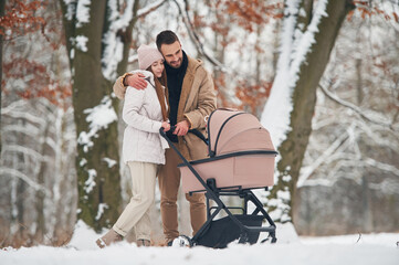 Mother and father with pram. Lovely couple have a walk in the winter forest