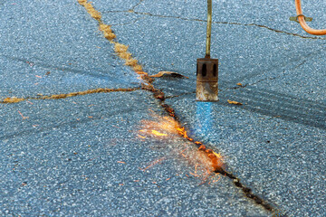 Worker performs road surface restoration work by burning dry grass cracks asphalt before coating...