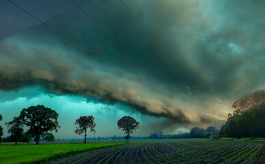 Fototapeta premium A formidable shelf cloud dominates the horizon in this image, signaling the imminent arrival of a powerful storm over a serene farmland. The dark, undulating base of the cloud contrasts with the