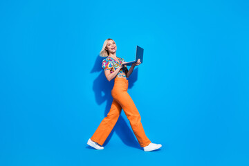 Full body profile photo of positive pretty lady walk use wireless laptop empty space isolated on blue color background
