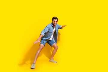 Full body photo of funky handsome man dressed denim shirt shorts surfing on imaginary board isolated on vivid yellow color background