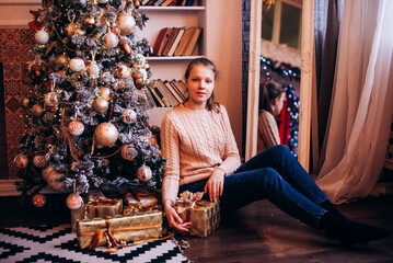 Teenage girl with gift box near Christmas tree on Christmas eve at home. celebration concept