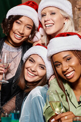 portrait of excited multiracial women with champagne looking at camera in bar, Christmas party