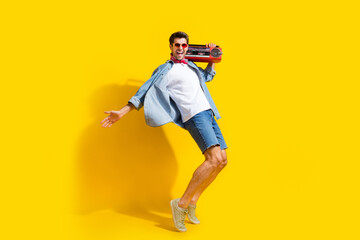Fototapeta na wymiar Full body photo of nice man dressed denim shirt hold boombox on shoulder dancing at summer retro party isolated on yellow color background