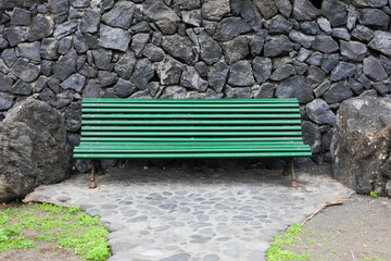 Bench in park. Green paint wooden bench on promenade. Tenerife Canary island. Black rock wall. Volcanic stones decoration.