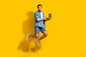 Fototapeta na wymiar Full body photo of intelligent man dressed denim shirt flying with fast internet speed on laptop isolated on yellow color background