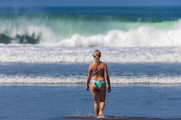 A young woman is walking on the beach with big waves, Seminyak, Bali Island, Indonesia