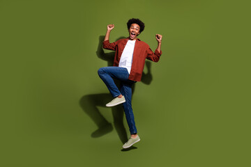 Fototapeta na wymiar Full size photo of handsome young guy jump raise fists excited scream dressed stylish brown outfit isolated on khaki color background