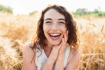 Happy beautiful woman smiling at camera in a wheat field - Delightful female enjoying summertime sunny day outside - Wellbeing concept with confident girl laughing in the nature