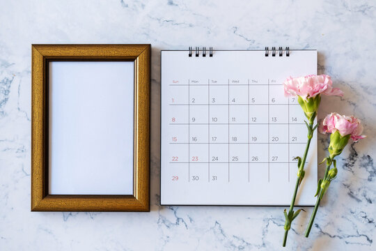 Carnation flower on blank picture frame and calendar on marble background, Valentine's Day, Mother's Day or Birthday background