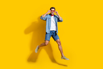 Fototapeta na wymiar Full body photo of funky optimistic man dressed denim shirt shorts jumping touching glasses isolated on vivid yellow color background.