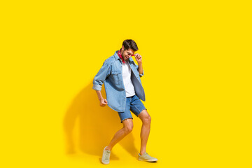 Full body photo of good mood cool man dressed denim shirt shorts touching glasses dancing isolated on vibrant yellow color background
