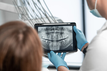 The dentist shows the results of panoramic tomography of the patient's teeth on a tablet. The...