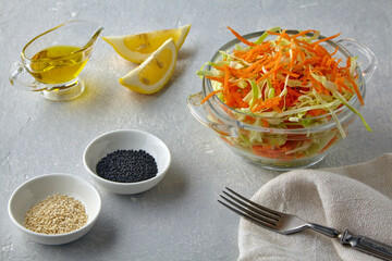 Vegetable salad of cabbage, carrots and cumin and sesame seeds dressed with olive oil and lemon in a glass bowl on a light stone table